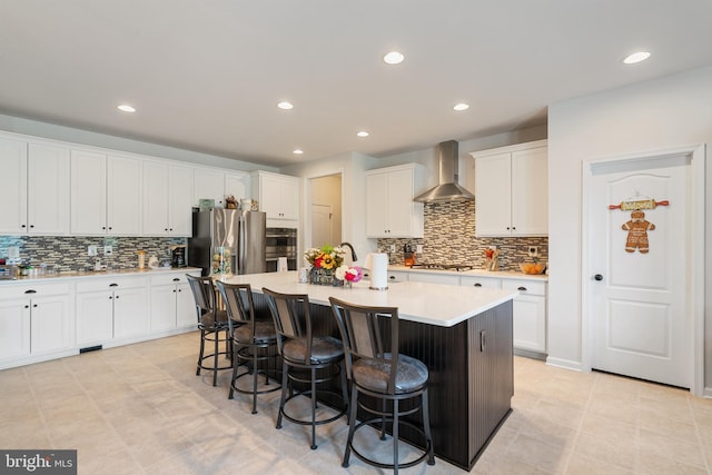 kitchen featuring wall chimney range hood, backsplash, appliances with stainless steel finishes, a breakfast bar area, and recessed lighting