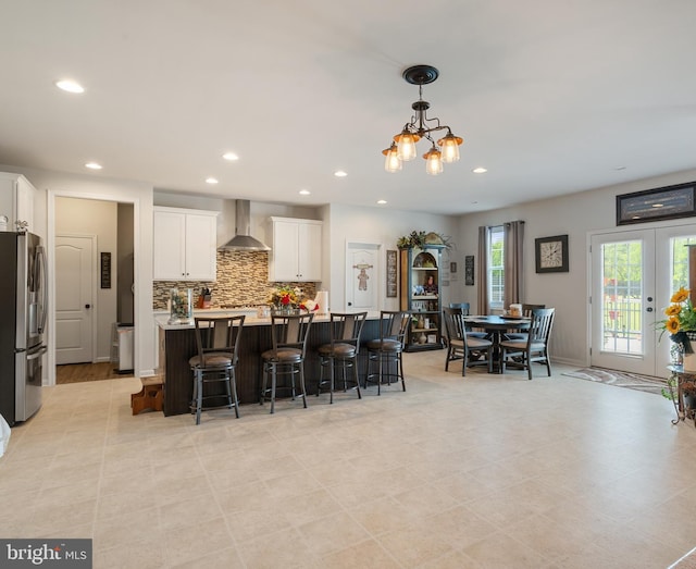 kitchen featuring stainless steel fridge, wall chimney range hood, white cabinetry, recessed lighting, and decorative backsplash