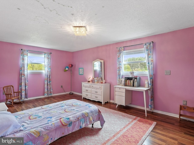bedroom featuring multiple windows, wood finished floors, a textured ceiling, and baseboards