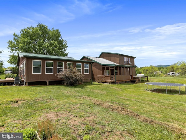 back of property featuring a trampoline, central AC unit, a lawn, a deck, and metal roof