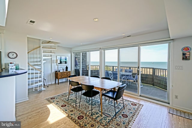 dining room featuring light wood finished floors, a water view, baseboards, stairway, and recessed lighting