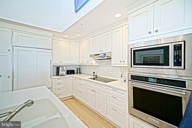 kitchen with stainless steel appliances, a skylight, white cabinets, light countertops, and light wood-style flooring