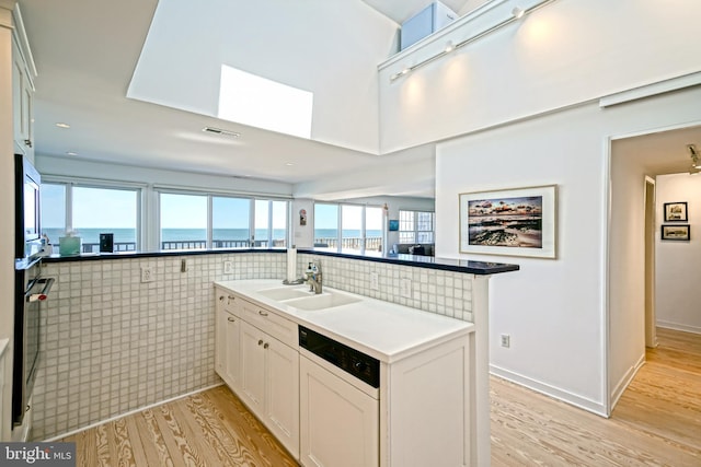 kitchen featuring a sink, dishwashing machine, light wood-style floors, white cabinetry, and stainless steel oven