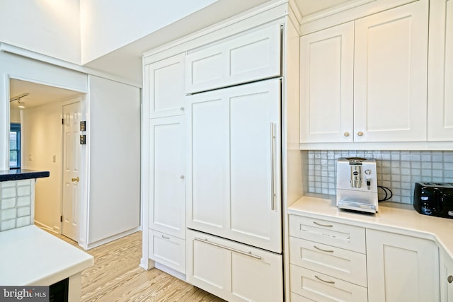 kitchen with paneled refrigerator, white cabinets, backsplash, light wood-style floors, and light countertops