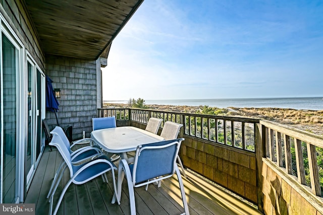 balcony with outdoor dining area and view of water and beach
