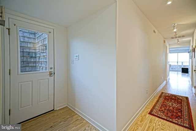 hallway featuring rail lighting, light wood-type flooring, and baseboards