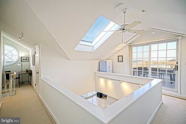 hallway with lofted ceiling, a skylight, light carpet, and baseboards