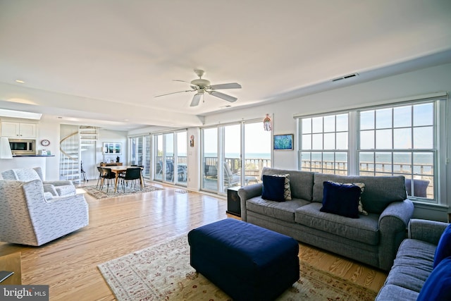 living area with a ceiling fan, light wood-type flooring, and stairway