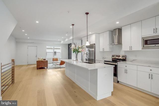 4902 D St SE, Washington, DC 20019 - kitchen featuring stainless steel appliances, wall chimney range hood, light wood-style flooring, a sink, and white cabinetry