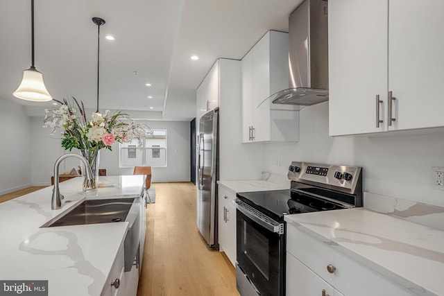 4902 D St SE, Washington, DC 20019 - kitchen featuring stainless steel appliances, wall chimney exhaust hood, light wood-type flooring, white cabinetry, and pendant lighting
