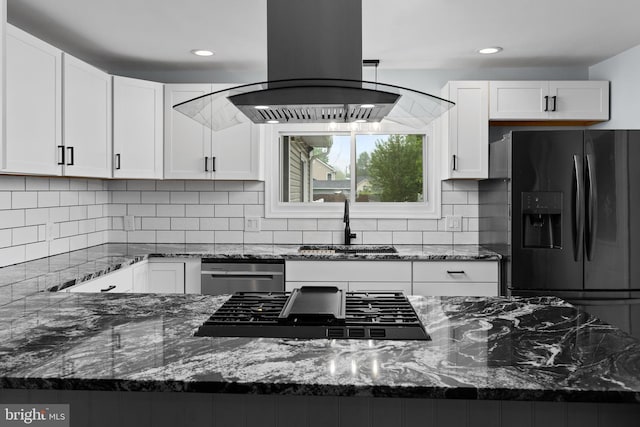 kitchen featuring stovetop, black fridge, island range hood, dark stone counters, and recessed lighting