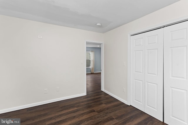 unfurnished bedroom with dark wood-style floors, baseboards, and a closet