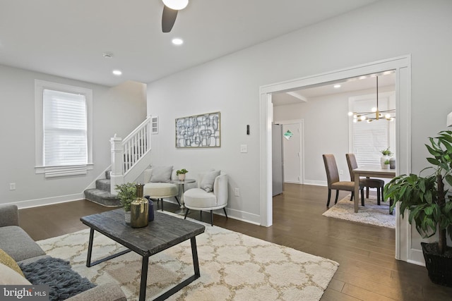 living room with stairs, a chandelier, dark wood-style floors, a ceiling fan, and baseboards