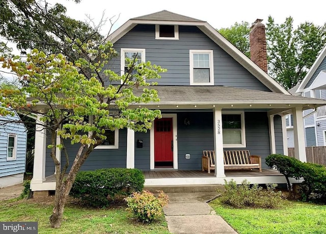 view of front facade featuring covered porch, a chimney, and roof with shingles