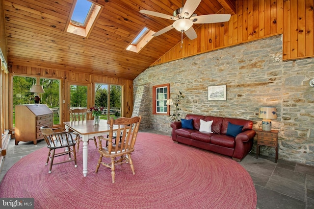 dining area with wooden ceiling, ceiling fan, wood walls, high vaulted ceiling, and a skylight
