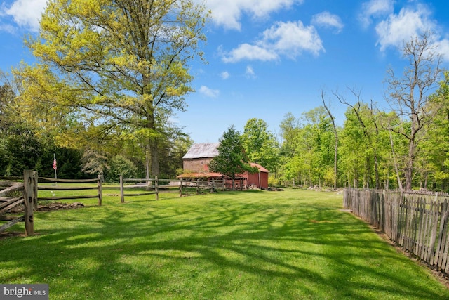 view of yard with a wooded view, fence, an outbuilding, and a barn