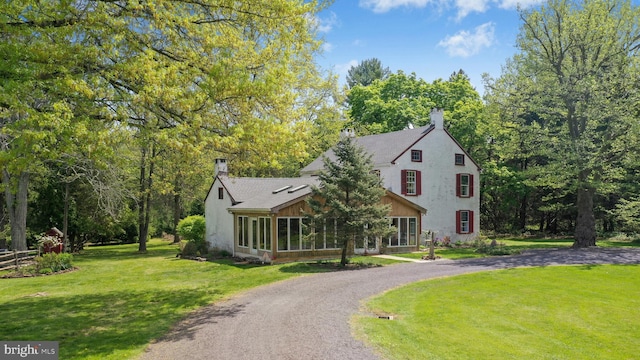 view of front facade with a sunroom, stucco siding, a chimney, curved driveway, and a front yard