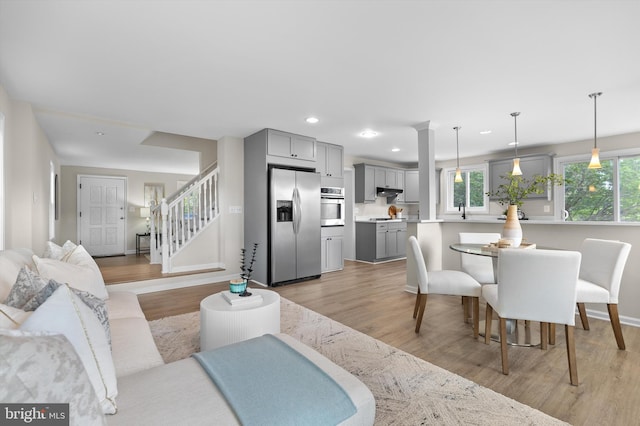 living room with light wood finished floors, plenty of natural light, recessed lighting, stairs, and baseboards