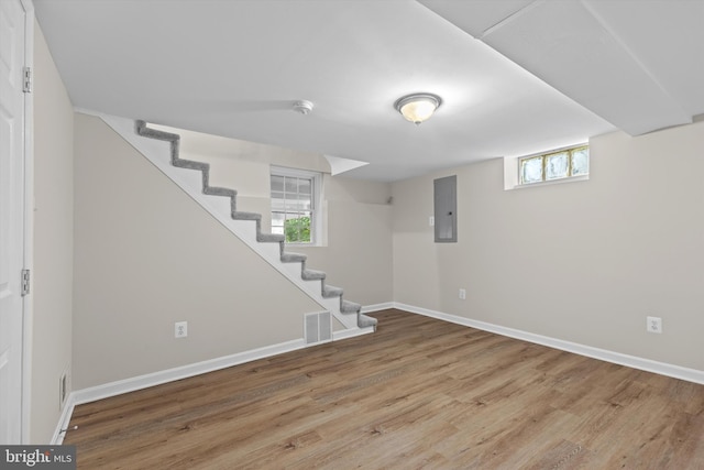 basement featuring wood finished floors, baseboards, stairway, and electric panel