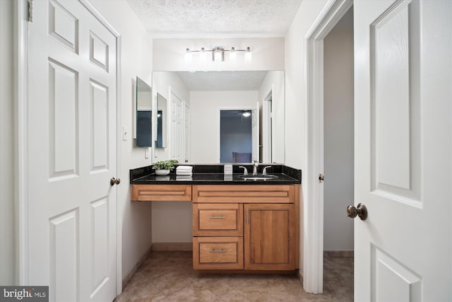 bathroom with a textured ceiling, vanity, tile patterned floors, and baseboards