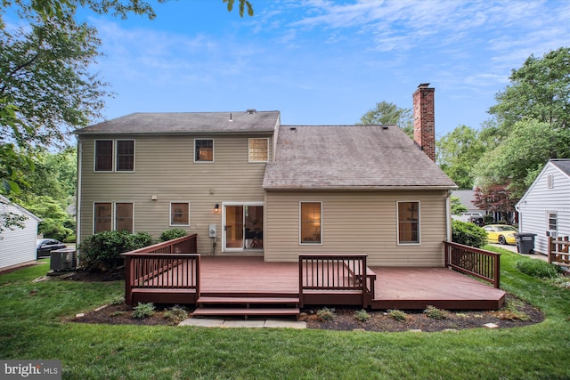 rear view of house featuring a chimney, a lawn, a deck, and roof with shingles