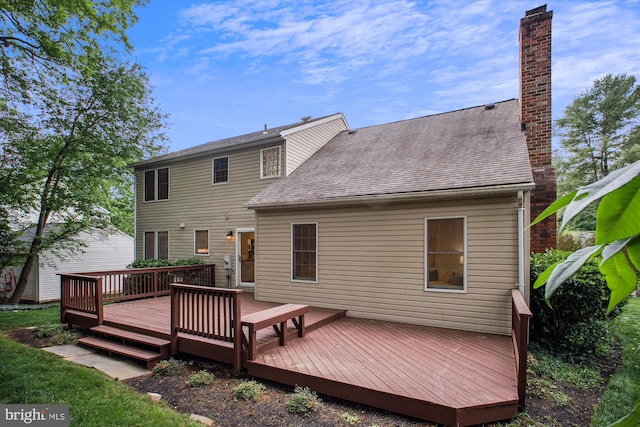 rear view of house with a chimney, a wooden deck, and roof with shingles