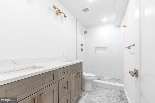 full bath with double vanity, toilet, a tile shower, a sink, and visible vents