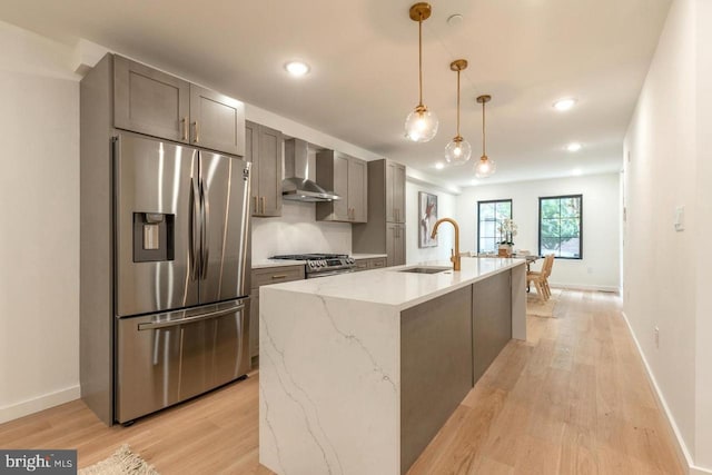 kitchen featuring light wood-style flooring, baseboards, a sink, wall chimney range hood, and appliances with stainless steel finishes