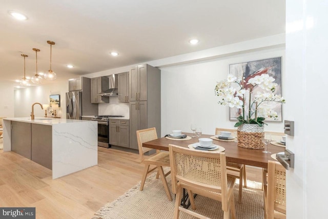 kitchen with light wood-style flooring, a sink, wall chimney exhaust hood, gray cabinets, and appliances with stainless steel finishes