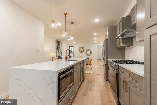 kitchen featuring a sink, stainless steel appliances, gray cabinets, a kitchen island with sink, and light wood-type flooring