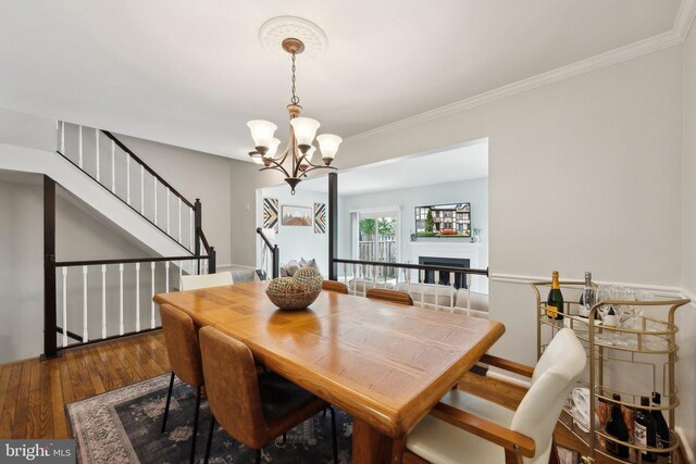 dining room with a chandelier, wood finished floors, ornamental molding, stairs, and a fireplace