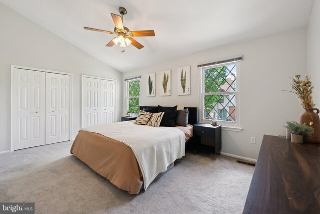carpeted bedroom with multiple closets, lofted ceiling, baseboards, and a ceiling fan