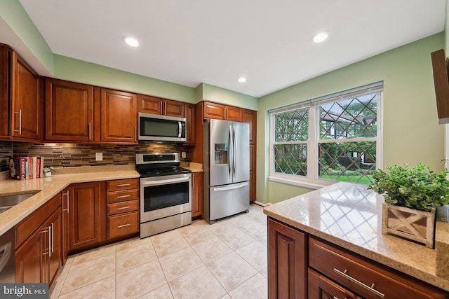 kitchen featuring stainless steel appliances, tasteful backsplash, light stone counters, light tile patterned floors, and brown cabinets