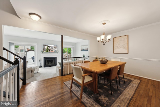 dining space featuring crown molding, plenty of natural light, wood-type flooring, a chandelier, and a fireplace