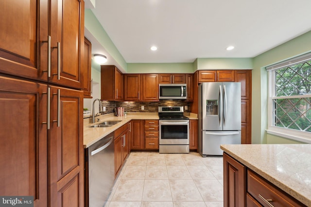kitchen featuring appliances with stainless steel finishes, a sink, tasteful backsplash, light tile patterned flooring, and brown cabinets