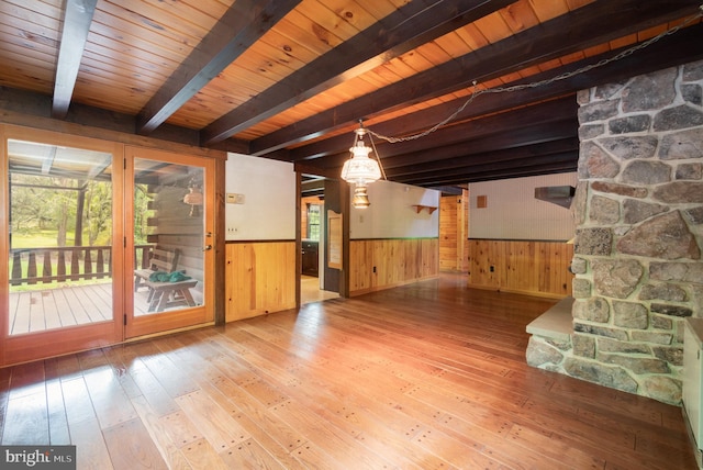 unfurnished living room with hardwood / wood-style flooring, beamed ceiling, a healthy amount of sunlight, and wood walls