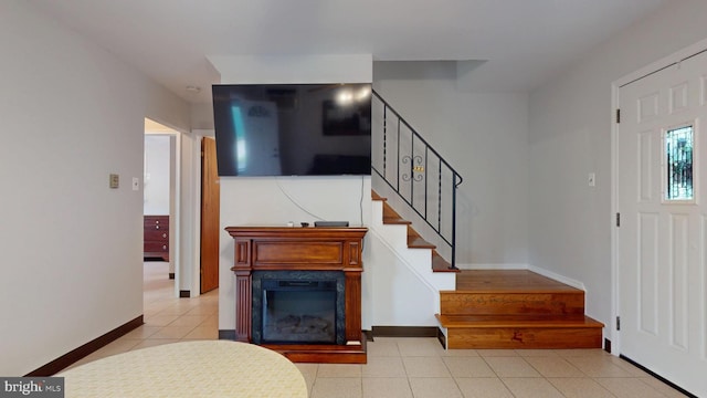 foyer entrance with stairway, baseboards, light tile patterned floors, and a glass covered fireplace