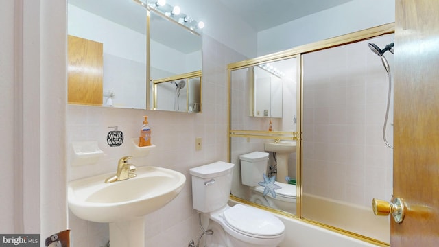 full bath with tile walls, toilet, shower / bath combination with glass door, and a sink