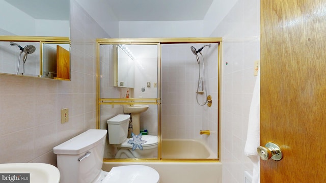 bathroom with toilet, tile walls, and bath / shower combo with glass door