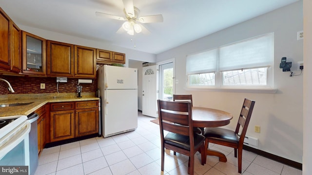 kitchen with brown cabinetry, white appliances, light stone counters, and a sink