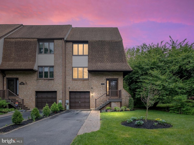 view of front of house featuring driveway, a shingled roof, an attached garage, a lawn, and brick siding