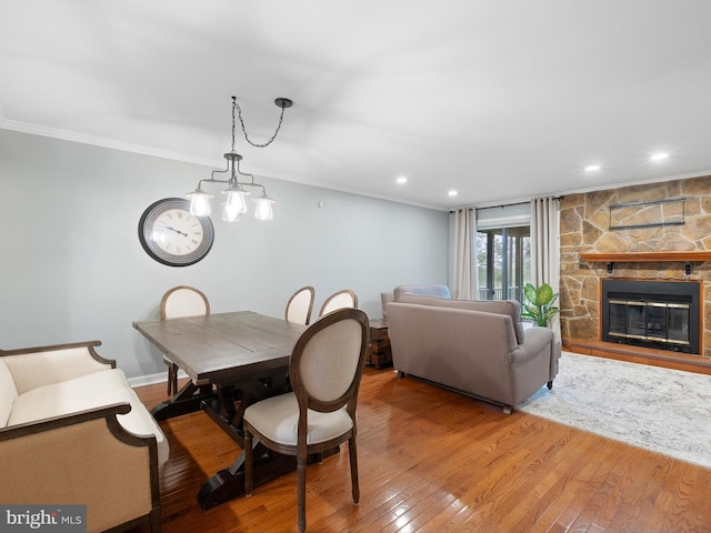 dining room with wood-type flooring, crown molding, a stone fireplace, recessed lighting, and a chandelier