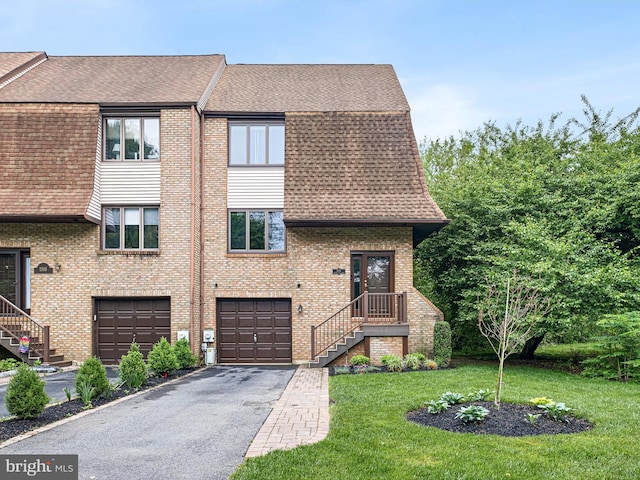 view of front of house with an attached garage, roof with shingles, driveway, a front yard, and brick siding