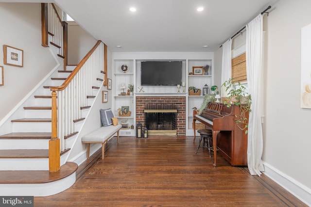 living room featuring wood finished floors, stairway, recessed lighting, a brick fireplace, and baseboards