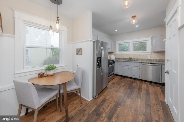 kitchen featuring appliances with stainless steel finishes, a sink, dark wood finished floors, light stone counters, and hanging light fixtures