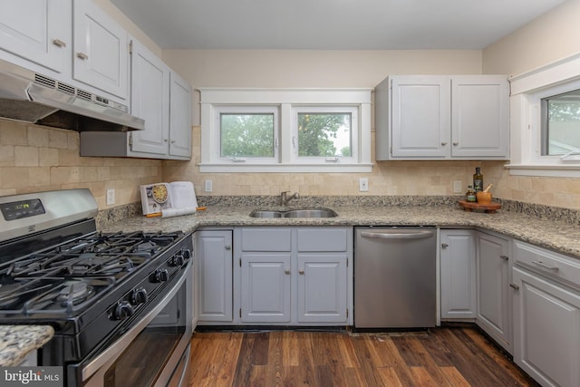 kitchen with stainless steel appliances, under cabinet range hood, a sink, dark wood-type flooring, and decorative backsplash