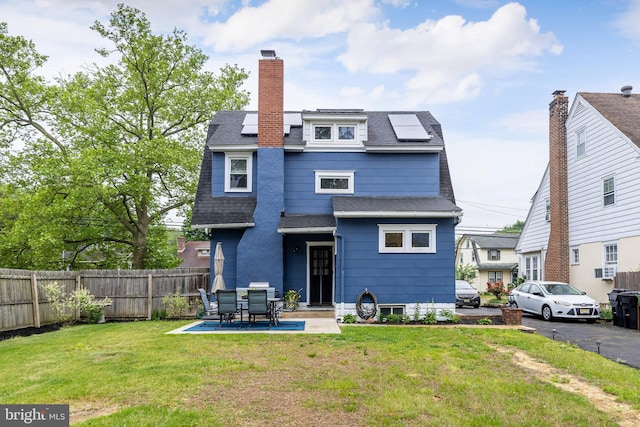 back of house featuring roof mounted solar panels, a chimney, roof with shingles, and a patio area