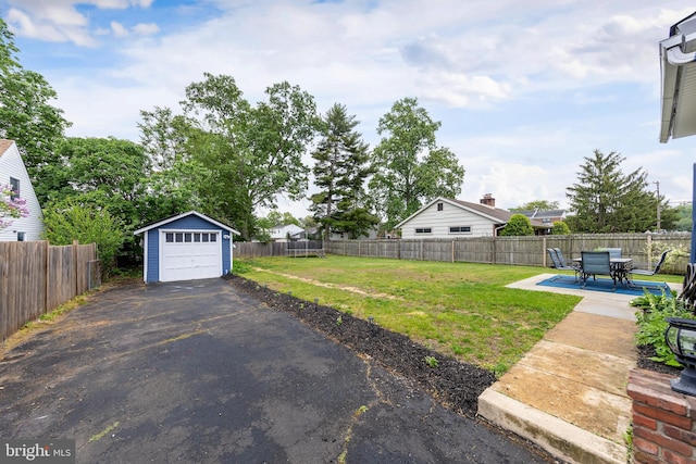 view of yard with an outdoor structure, asphalt driveway, a detached garage, a patio, and a storage unit