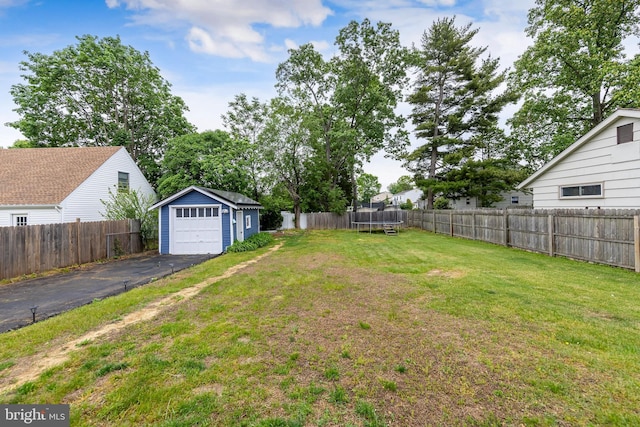 view of yard featuring a trampoline, an outbuilding, asphalt driveway, and a garage