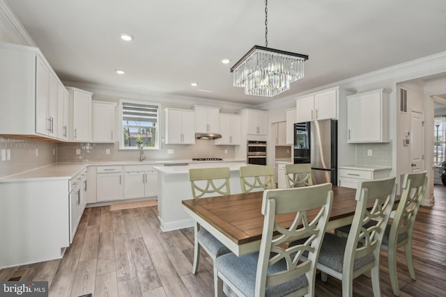 kitchen with a center island, stainless steel appliances, backsplash, under cabinet range hood, and ornamental molding